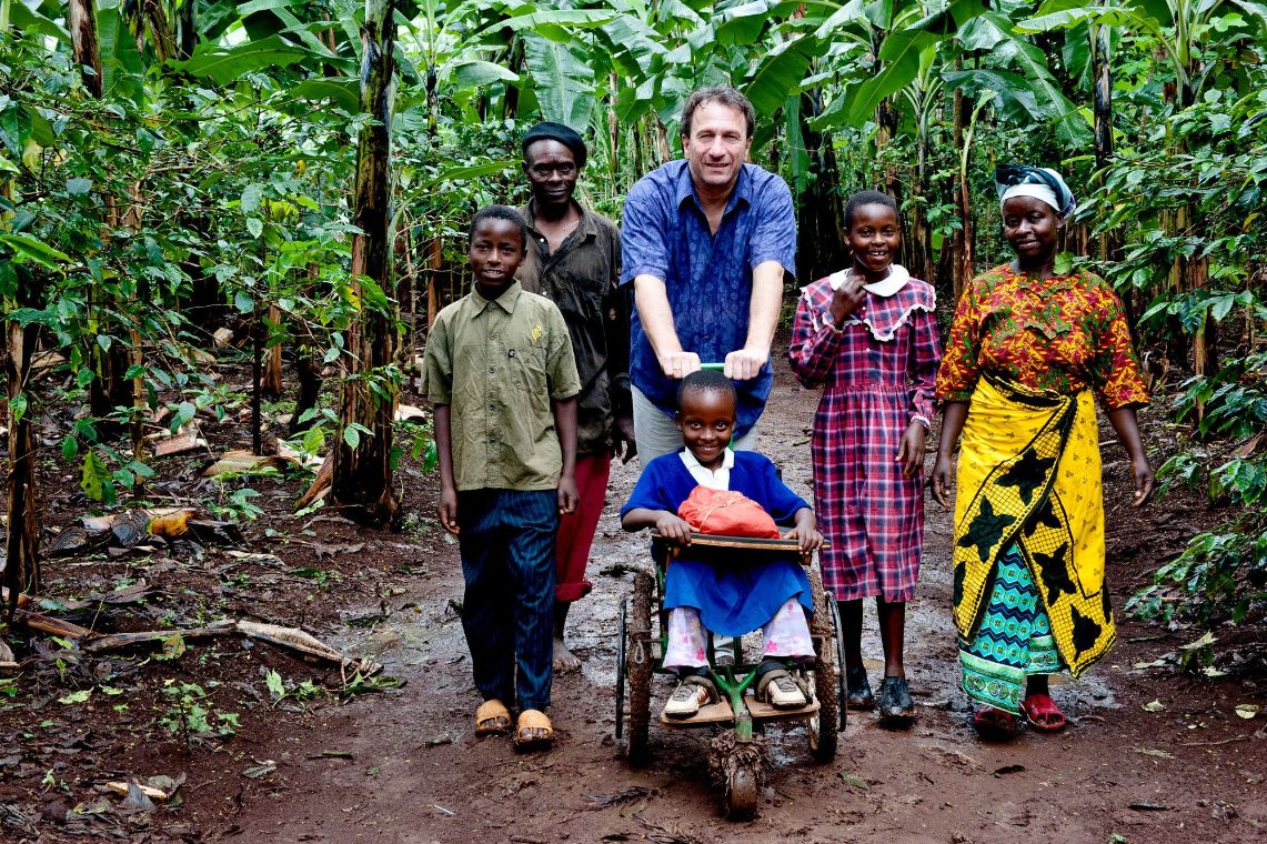 Eine afrikanische Familie mit einem Besucher aus Deutschland, der ein Kind der Familie im Rollstuhl schiebt.