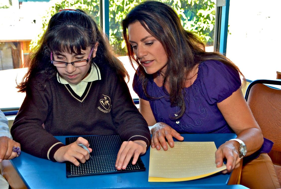 Eine Frau und ein Mädchen am Schreibtisch mit Blindenschriftschablone