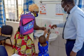 Afrikanische Frau mit Mund-Nasen-Schutz hilft einem kleinen Mädchen beim Händewaschen.