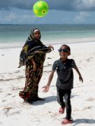 Ein lachender, etwa achtjähriger Junge mit Brille und eine Frau mit langem Gewand und Kopftuch an einem Sandstrand: Der Junge schaut einem Fußball nach, der fast über ihm fliegt.