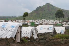 Ein Feld voller Zelte mit der Aufschrift UNHCR vor einem grünen, spitzen Hügel.
