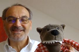 Ein Mann im weißen Hemd hält einen Plüschwolf hoch.