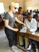 Frau mit Schirmmütze und Sonnenbrille im Klassenzimmer vor afrikanischen Schülern