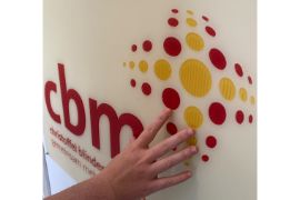 Auf dem Bild ist das Logo der CBM abgebildet. Eine Hand ertastet das Logo.