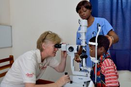 Eine Frau untersucht durch ein Gerät die Augen eines kleinen Jungen.