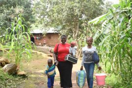 Zwei afrikanische Frauen und zwei Kinder auf einem Weg vor einer Hütte