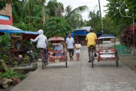 Vater und Tochter laufen durch den Straßenverkehr in einem philippinischen Dorf.