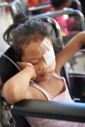 Kleines philippinisches Mädchen mit Augenverband sitzt im Rollstuhl