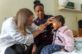 Deutsche Augenärztin untersucht kleine tansanische Patientin an den Augen