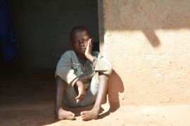 Ein Junge mit nach innen gekrümmten Füßen sitzt vor einer Hütte