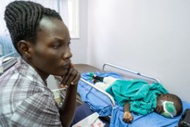 Mutter sitzt vor dem Krankenbett ihres Sohnes, der beide Augen verbunden hat.