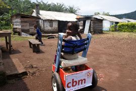 Kamerunisches Mädchen im Rollstuhl, auf dem &quot;gestiftet von der CBM&quot; steht.