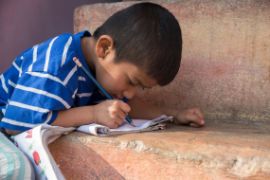 Nepalesischer Junge versucht, dicht über ein Heft gebeugt, etwas zu schreiben.