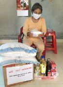 Eine Frau aus Asien sitzt vor einem Paket, auf dem zwei Säcke liegen. Daneben stehen Flaschen mit Öl und andere Lebensmittel.