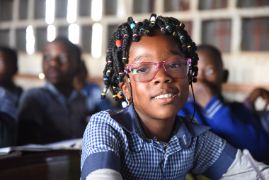 Ein Mädchen mit Brille sitzt in einem Klassenzimmer.