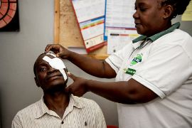 Ein afrikanischer Mann bekommt von einer Frau einen Augenverband angelegt.