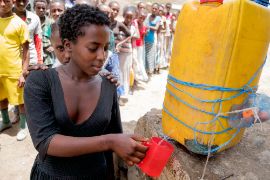 Eine junge afrikanische Frau zapft Wasser aus einem Kanister.