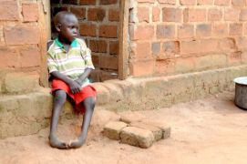Ein afrikanischer Junge mit Klumpfüßen sitzt an einem Hauseingang.