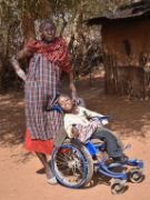 Kleiner Junge im Rollstuhl, dahinter steht eine Frau in Massai-Tracht.