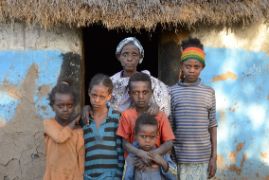 Eine ältere Frau und fünf Kinder von Kindergarten- bis zum Teenageralter stehen vor einer Hütte.