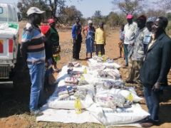 Lebensmittelpakete liegen auf dem Boden, Menschen stehen rundum, ein LKW parkt daneben. Dürre hat eine Hungerkrise in Simbabwe verursacht.