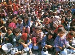 Am Boden sitzende Frauen und Kinder in afghanischer Tracht. Einige haben leere Blechtöpfe. Sie sind auf der Flucht vor Krieg.