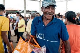 Ein lachender älterer Mann, dem rechts der Unterarm fehlt, trägt eine Tüte mit Lebensmitteln. Er erhielt sie, nachdem Taifun Haiyan Verwüstungen angerichtet hat.