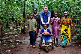 Eine afrikanische Familie mit einem Besucher aus Deutschland, der ein Kind der Familie im Rollstuhl schiebt.