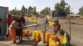 Kinder mit Wasserkanistern an einer Wasserpumpe