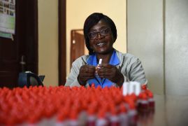 Eine lachende afrikanische Frau an einem Tisch voller kleiner Fläschchen