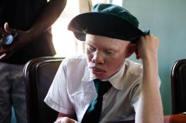 Junge mit Albinismus in Schuluniform am Schreibtisch im Klassenzimmer.