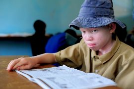 Junge mit Albinismu liest am Schulpult in einem aufgeschlagenen Heft