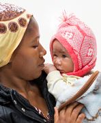 Junge afrikanische Frau hält ein Baby mit Mütze auf dem Arm