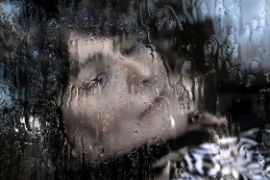 Gesicht einer Frau hinter einer Glasscheibe voller Wassertropfen. Sie hat die Augen geschlossen. 