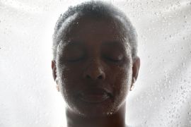Porträt einer afrikanischen Frau mit Wassertropfen im Gesicht vor einer Glasscheibe voller Wassertropfen.