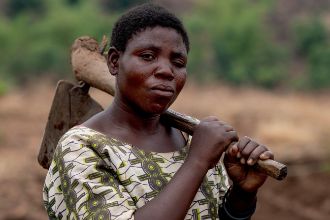 Eine afrikanische Frau trägt eine Hacke auf der Schulter.