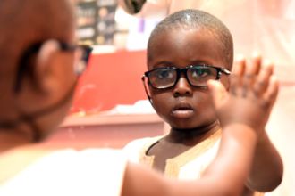 Afrikanischer Junge mit Brille schaut in den Spiegel