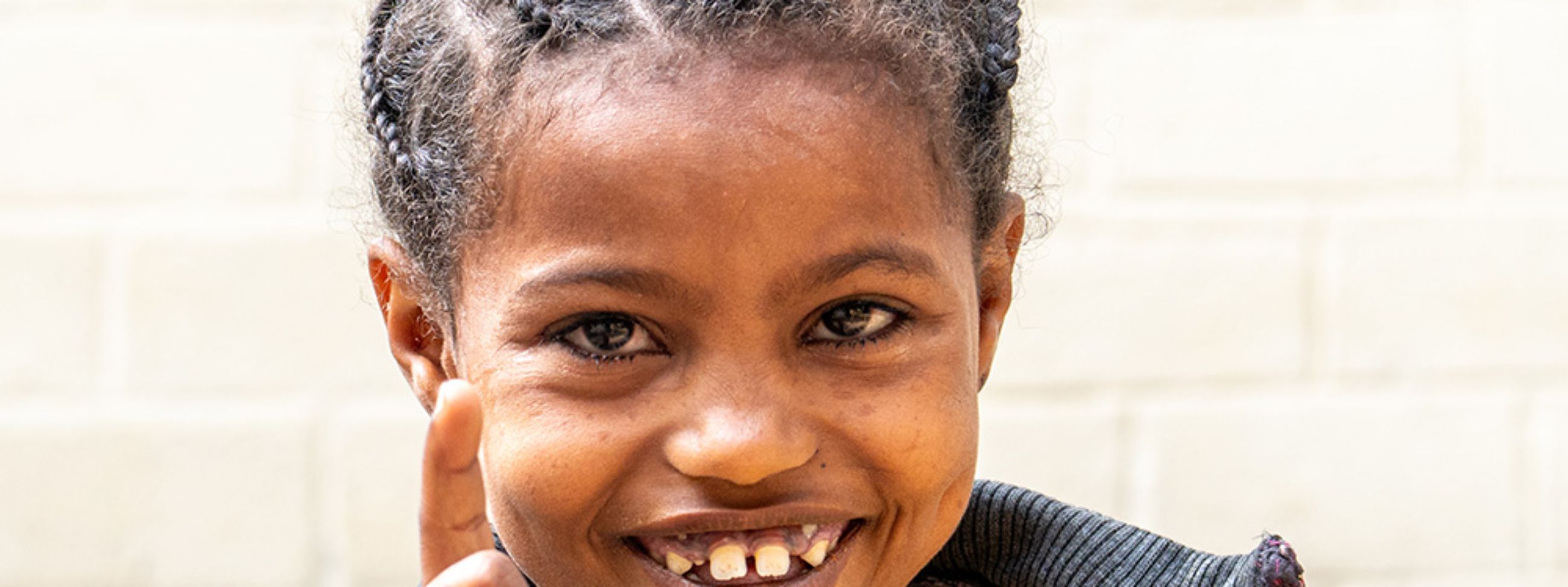 Ein etwa neunjähriges Mädchen steckt lachend den Zeigefinger hoch.