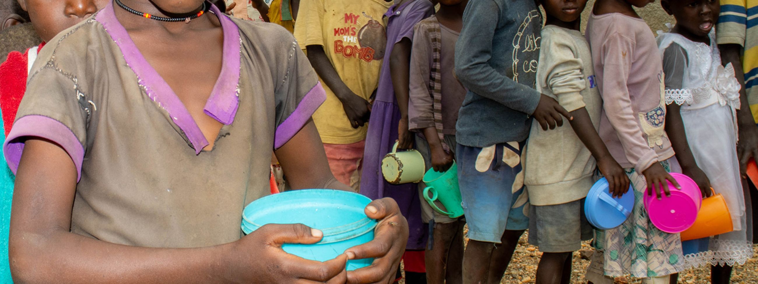 Zwei Reihen von Kindern stehen in der Schlange, in der Hand halten sie Plastikschüsselchen.