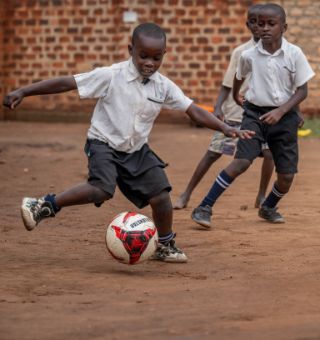 Drei etwa siebenjährige Jungen spielen Fußball in einem von einer Backsteinmauer begrenzten Hof.