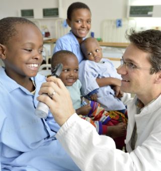 Ein Mann im weißen Kittel untersucht die Augen eines afrikanischen Mädchens