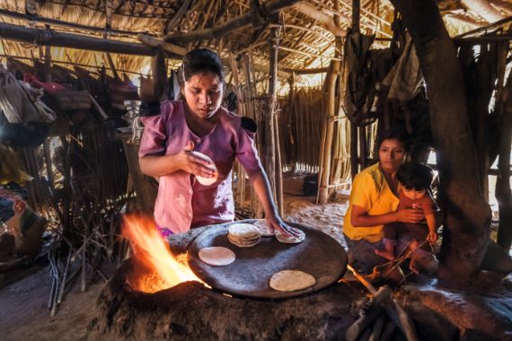 Frau macht Tortillas in einer Hütte über offenen Feuer