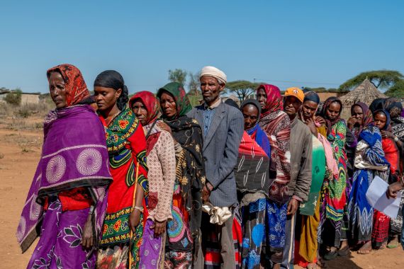 Bunt gekleidete Frauen und Kinder sowie zwei Männer stehen in einer Reihe hintereinander.