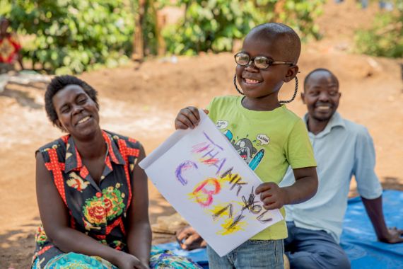 Ein kleiner afrikanischer Junge mit Brille hält ein Blatt Papier, auf dem steht: Thank you CBM!