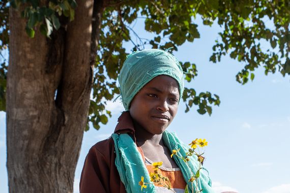Ein etwa zwölfjähriges Mädchen mit Kopftuch steht vor einem Baum.