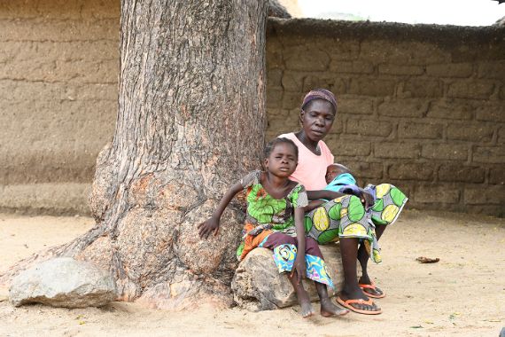 Eine Frau sitzt mit ihren beiden Kindern vor einem Baum.