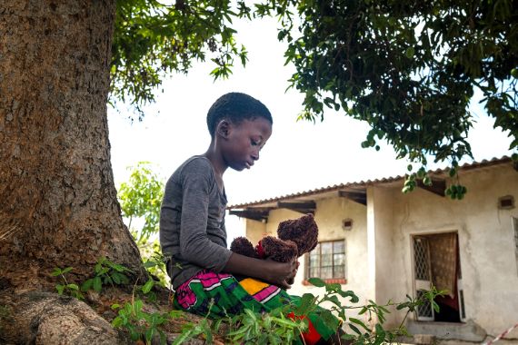 Ein Mädchen sitzt unter einem Baum und hält einen Teddybär in den Händen.