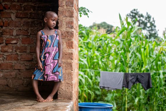 Ein kleines Mädchen mit O-Beinen steht auf einer Backsteinveranda.