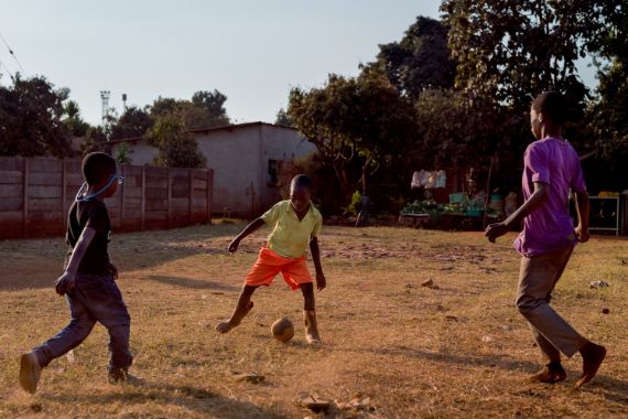 Drei Jungen spielen Fußball auf einer trockenen Wiese.