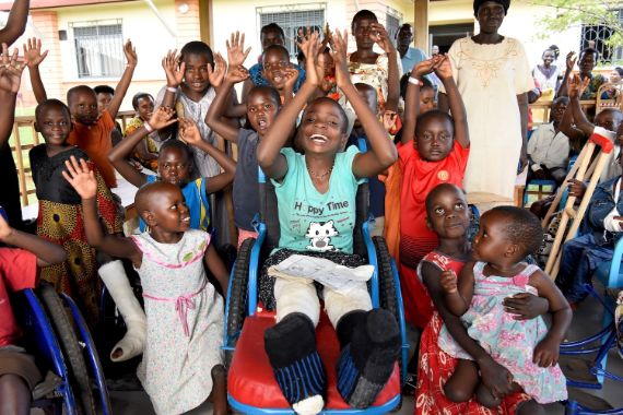 Eine Gruppe von Kindern reißt jubelnd die Arme hoch, einige haben einen Gipsverband oder sitzen im Rollstuhl.
